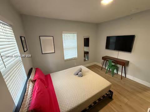 A bedroom features a bed with red pillows, a wall-mounted television, and a wooden desk — 6828 NW 3rd Ave # 1, Miami FL 33150, MIAMI, FL