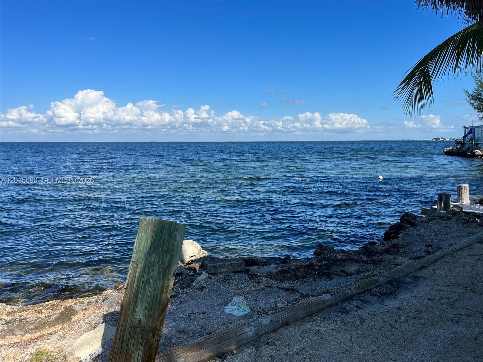 A wooden post stands on a rocky shoreline overlooking a calm, blue ocean — 103650 Overseas Hwy, Key Largo FL 33037, KEY LARGO, FL