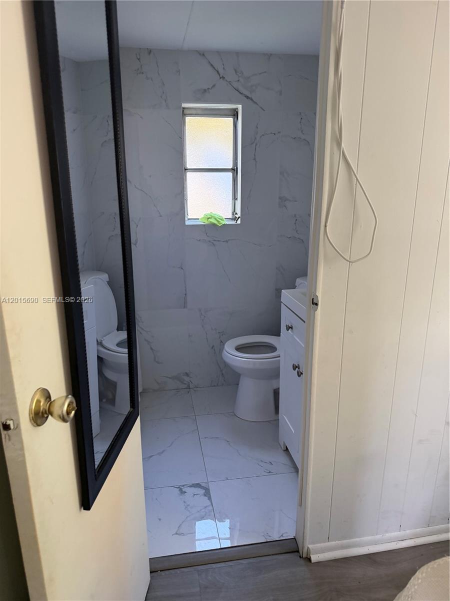 A small bathroom features white marble-patterned tile walls and floors, a toilet, and a vanity — 103650 Overseas Hwy, Key Largo FL 33037, KEY LARGO, FL