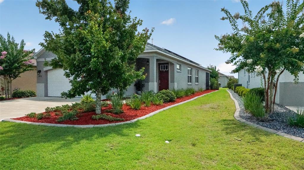 A single-story house with a red front door, a concrete driveway, and landscaped garden beds — 8750 SW 76TH STREET ROAD, OCALA, FL