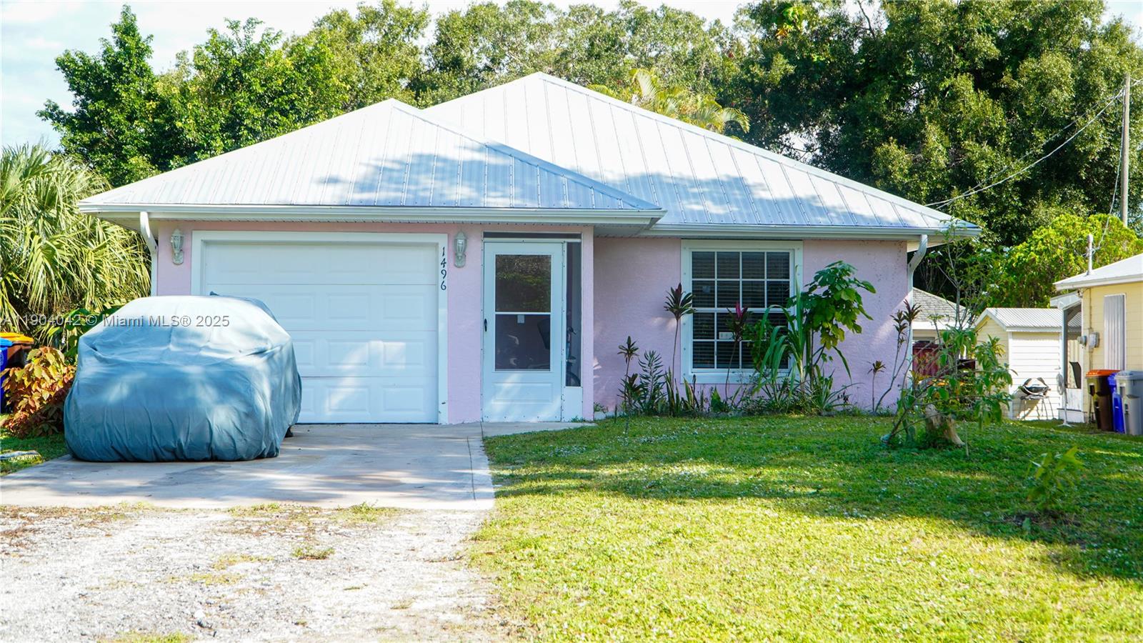 A single-story pink house with a metal roof, a garage, and a covered front entrance — 1496 SW 24th Ave SW, Vero Beach FL 32962, VERO BEACH, FL