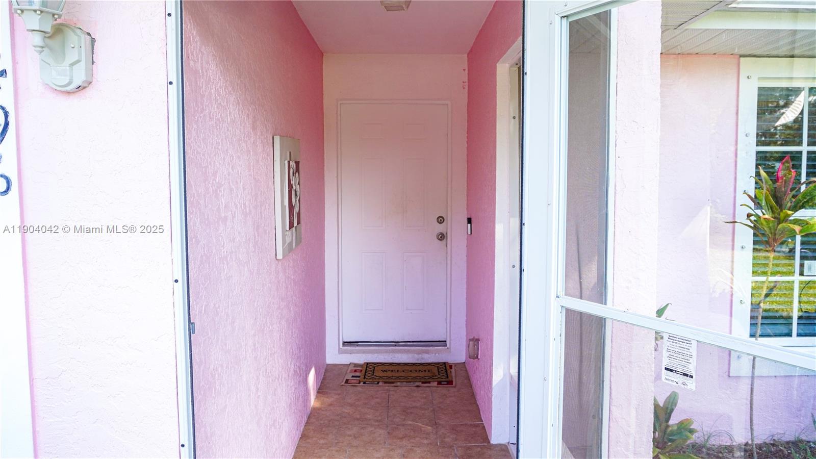 A pink-walled entryway features a white front door, tiled floor, and a welcome mat — 1496 SW 24th Ave SW, Vero Beach FL 32962, VERO BEACH, FL