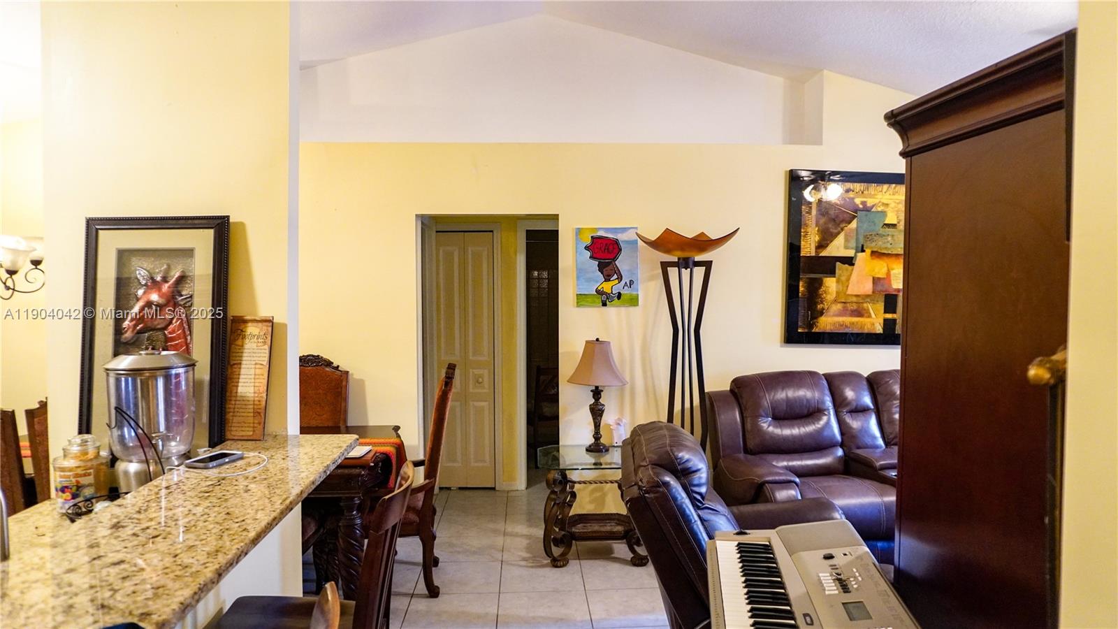 A living room with a vaulted ceiling, leather furniture, and a kitchen counter in foreground — 1496 SW 24th Ave SW, Vero Beach FL 32962, VERO BEACH, FL