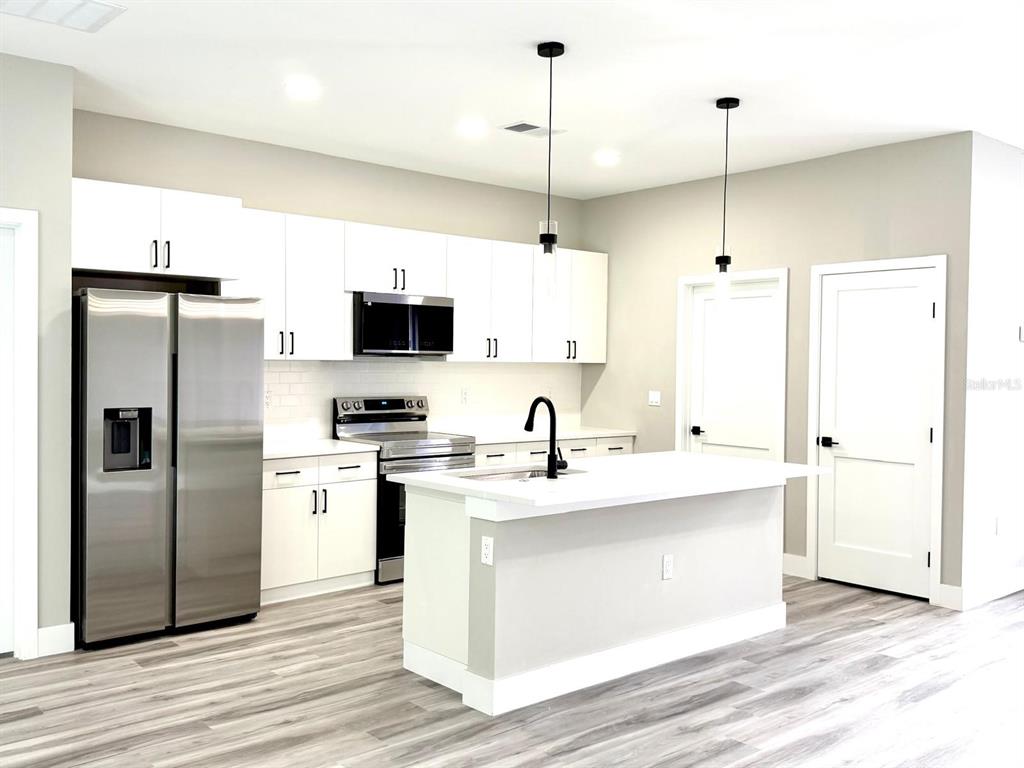 A modern kitchen features white cabinets, stainless steel appliances, a center island, and wood-look flooring — 1864 W ROSEBORO DRIVE, CITRUS SPRINGS, FL