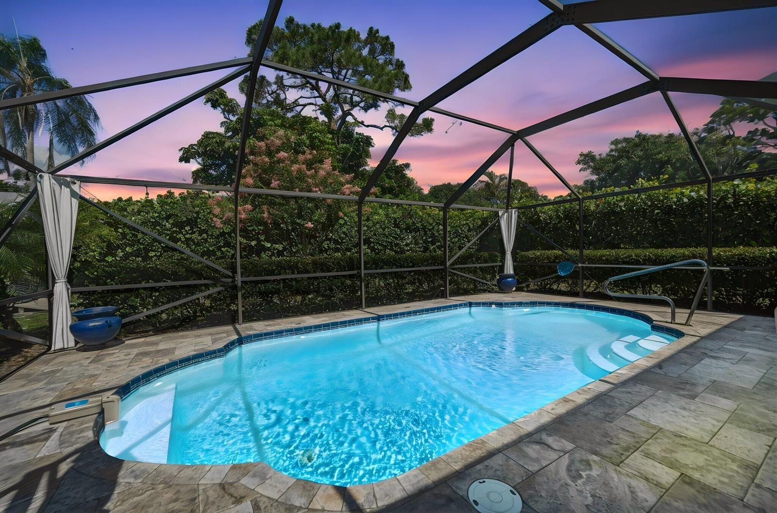 A screened-in swimming pool with stone decking and a sunset view in the background — 1252 SE Madison Avenue, Stuart FL 34996, STUART, FL