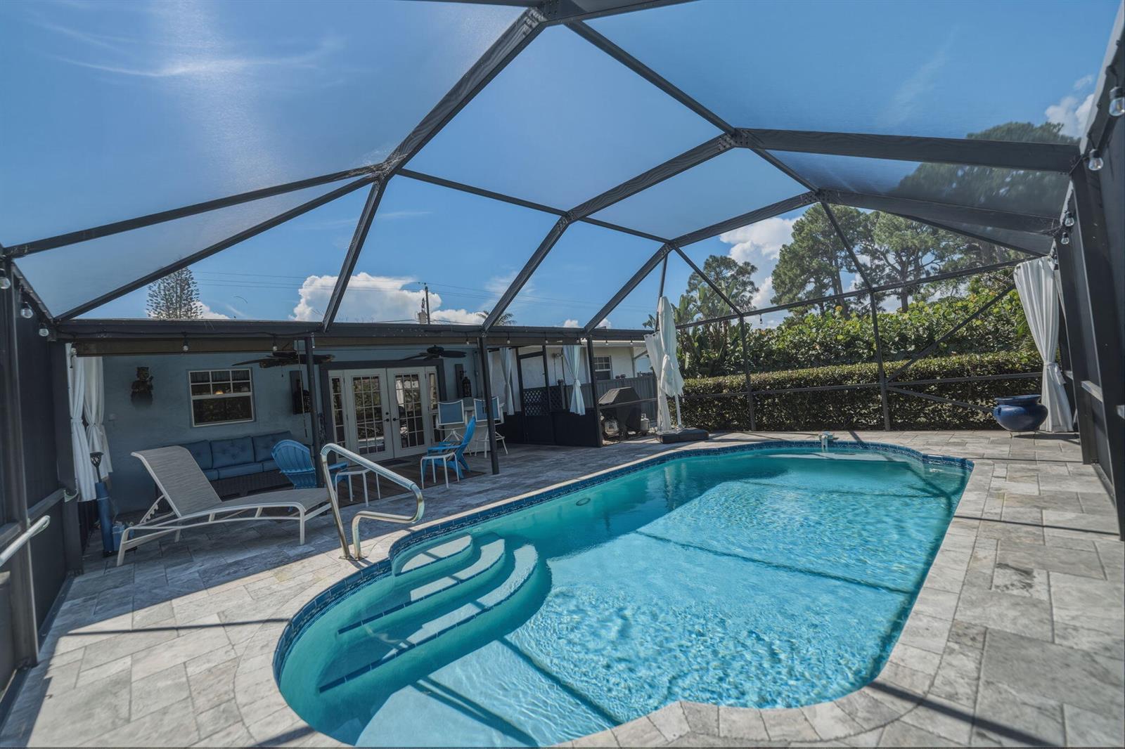 A screened-in patio features a swimming pool with steps and stone pavers under a roof — 1252 SE Madison Avenue, Stuart FL 34996, STUART, FL