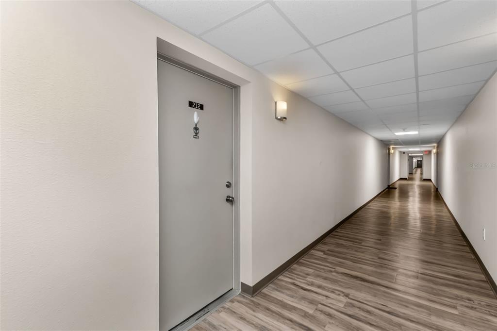 A long apartment hallway features light-colored walls, wood-look flooring, and a door labeled 212 — 21267 GERTRUDE AVENUE UNIT 212, PORT CHARLOTTE, FL