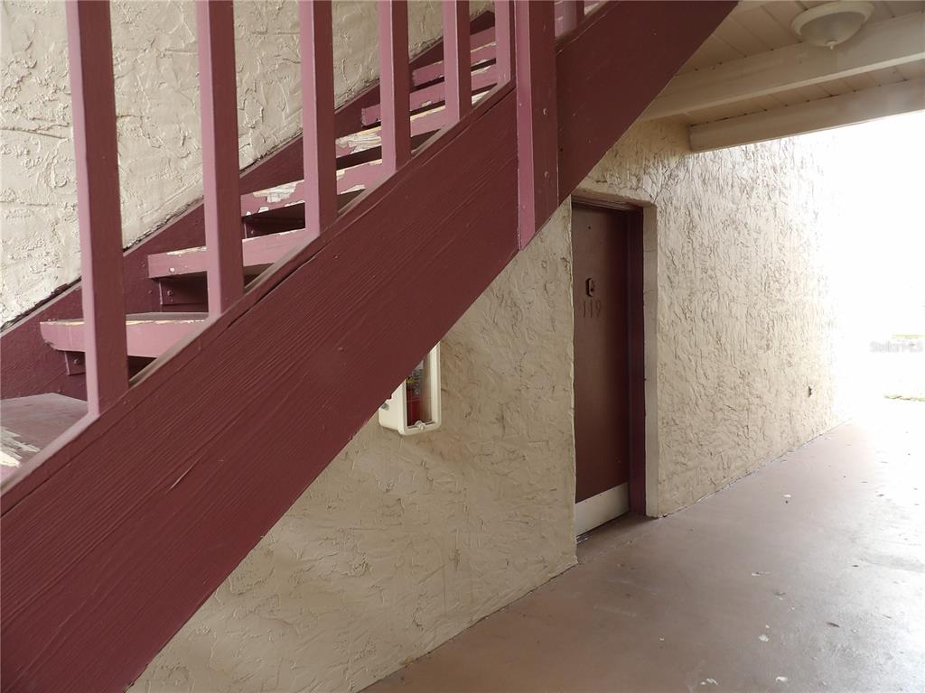 A brown door labeled 119 sits beneath a wooden staircase on a textured exterior wall — 3836 N LAKE DRIVE UNIT 119, TAMPA, FL