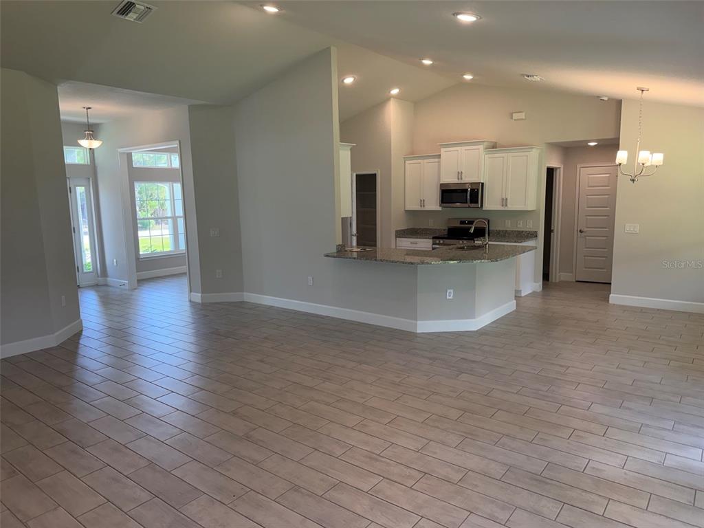 An open-concept kitchen with white cabinets and granite countertops overlooks a spacious tiled living area — 17433 EDGEWATER DRIVE, PORT CHARLOTTE, FL
