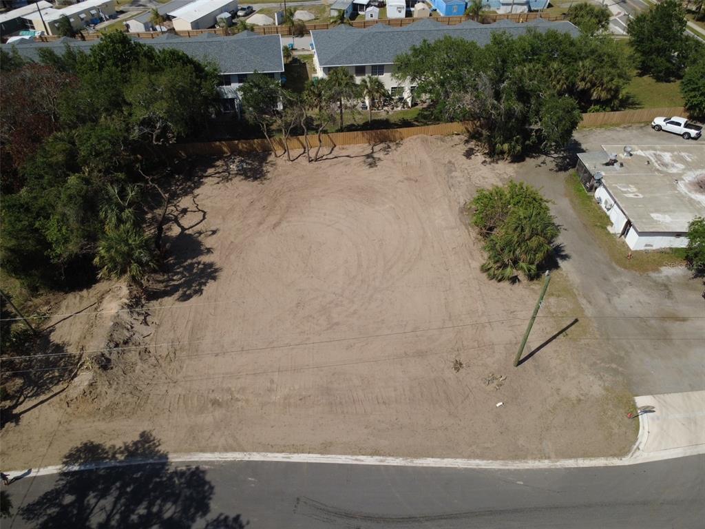 An aerial view shows a cleared, sandy vacant lot bordered by trees and nearby buildings — OAK LANE, CAPE CANAVERAL, FL
