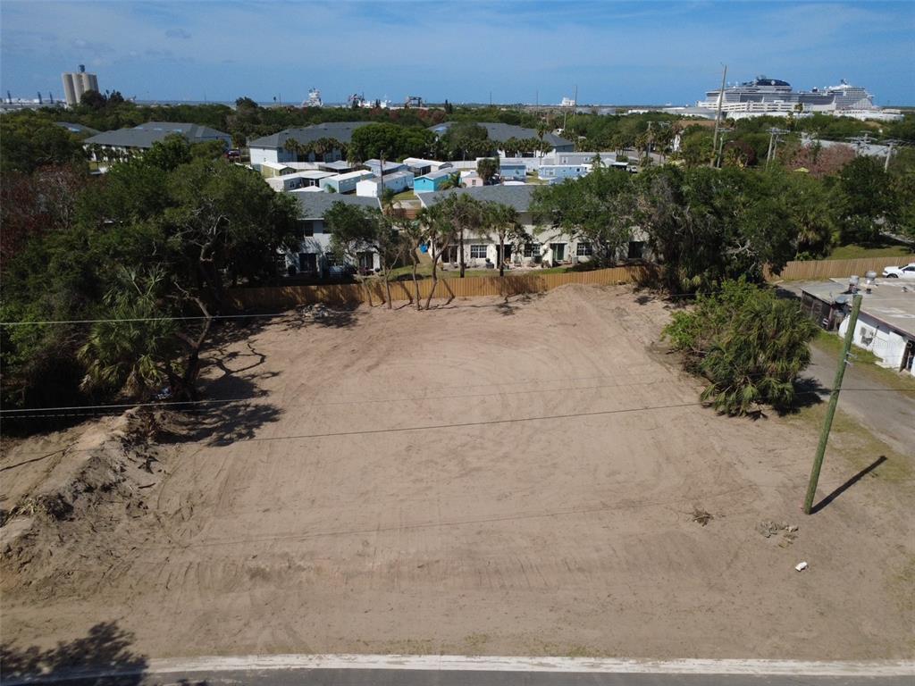An aerial view shows a cleared, sandy vacant lot bordered by trees and residential buildings — OAK LANE, CAPE CANAVERAL, FL