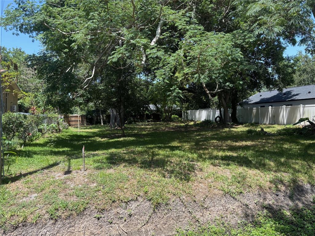 A grassy, tree-shaded vacant lot is enclosed by a white vinyl fence — 9674 8TH AVENUE, ORLANDO, FL