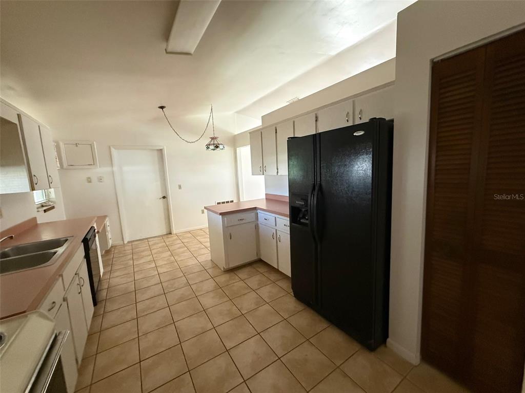 A kitchen features white cabinets, pink laminate countertops, a black refrigerator, and tiled flooring — 9706 SW 30TH TERRACE, OCALA, FL