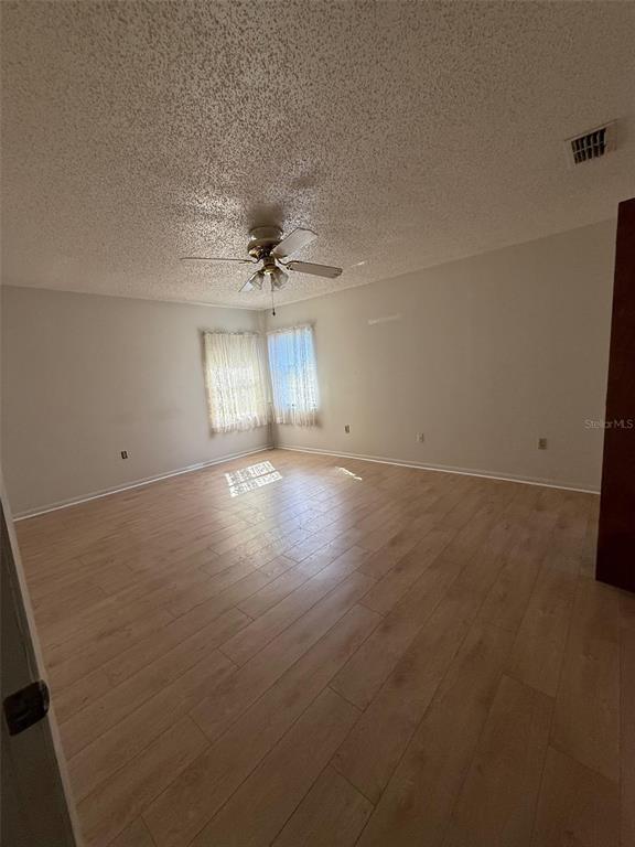 An empty room with light wood-look flooring, a ceiling fan, and two windows with curtains — 9706 SW 30TH TERRACE, OCALA, FL