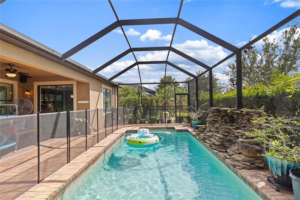 A screened-in swimming pool with a stone water feature and a safety fence — 743 WELLINGTON COURT, OLDSMAR, FL