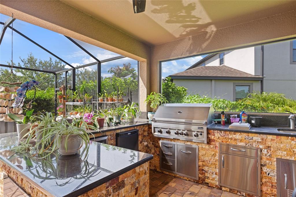 An outdoor kitchen with a stainless steel grill, stone veneer base, and granite countertops — 743 WELLINGTON COURT, OLDSMAR, FL