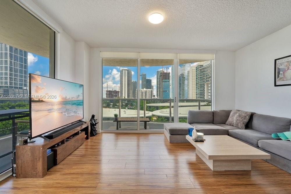 A living room features wood flooring, a large sectional sofa, and floor-to-ceiling windows with city views — 601 NE 23rd St # 1406, Miami FL 33137, MIAMI, FL