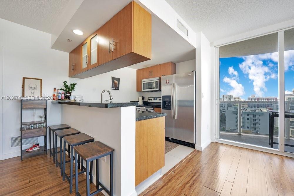 A kitchen with wood cabinets, stainless steel appliances, and a breakfast bar with stools — 601 NE 23rd St # 1406, Miami FL 33137, MIAMI, FL