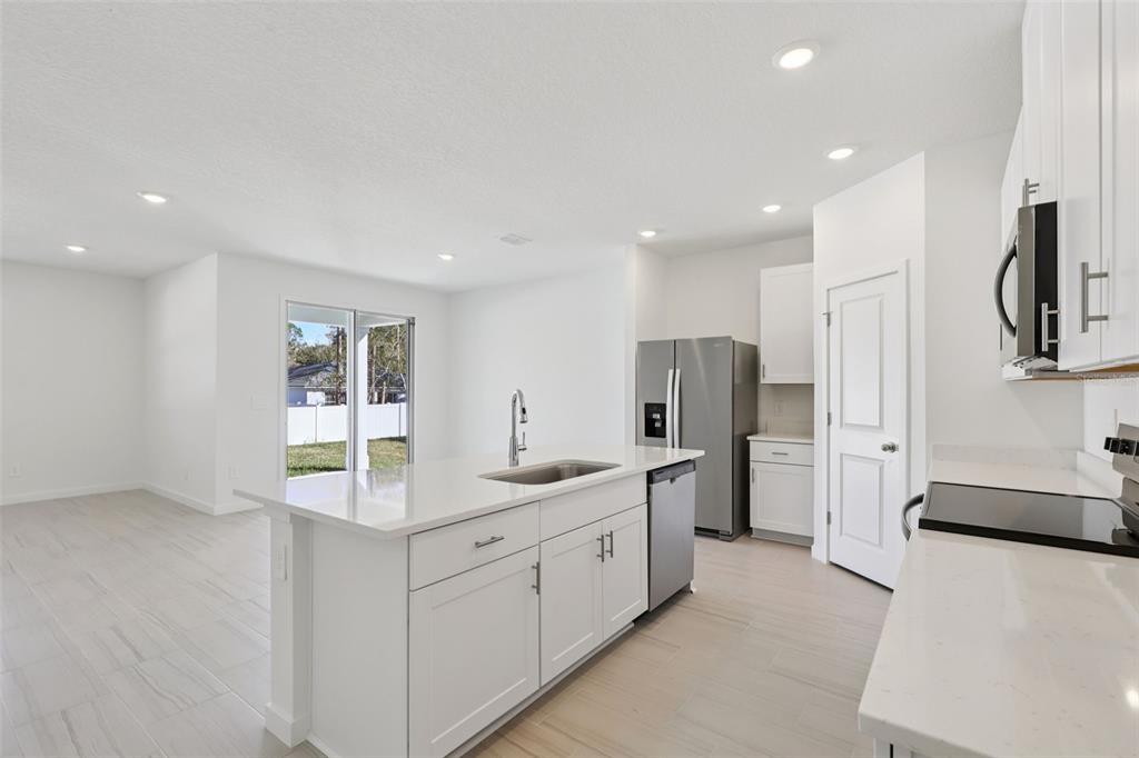 A modern kitchen features white cabinets, quartz countertops, a center island, and light tile flooring — 51 WANDERING CREEK WAY, PALM COAST, FL