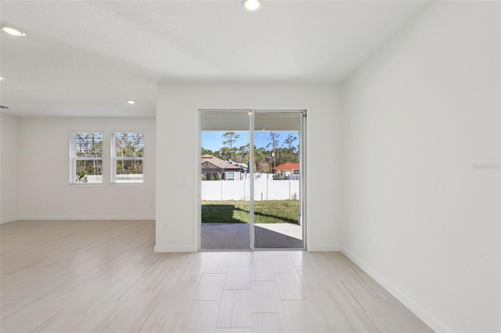 A bright, empty room features light-colored tile flooring, white walls, and sliding glass patio doors — 51 WANDERING CREEK WAY, PALM COAST, FL