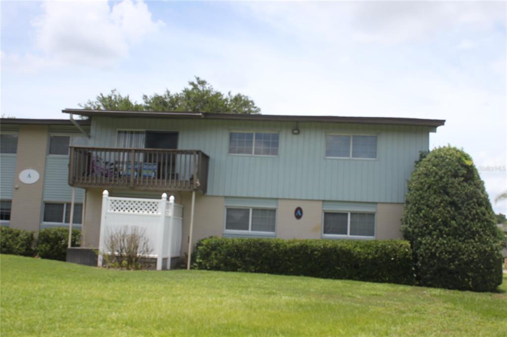 A two-story apartment building features a wooden balcony, white privacy fencing, and green landscaping — 1695 LEE ROAD UNIT A101, WINTER PARK, FL