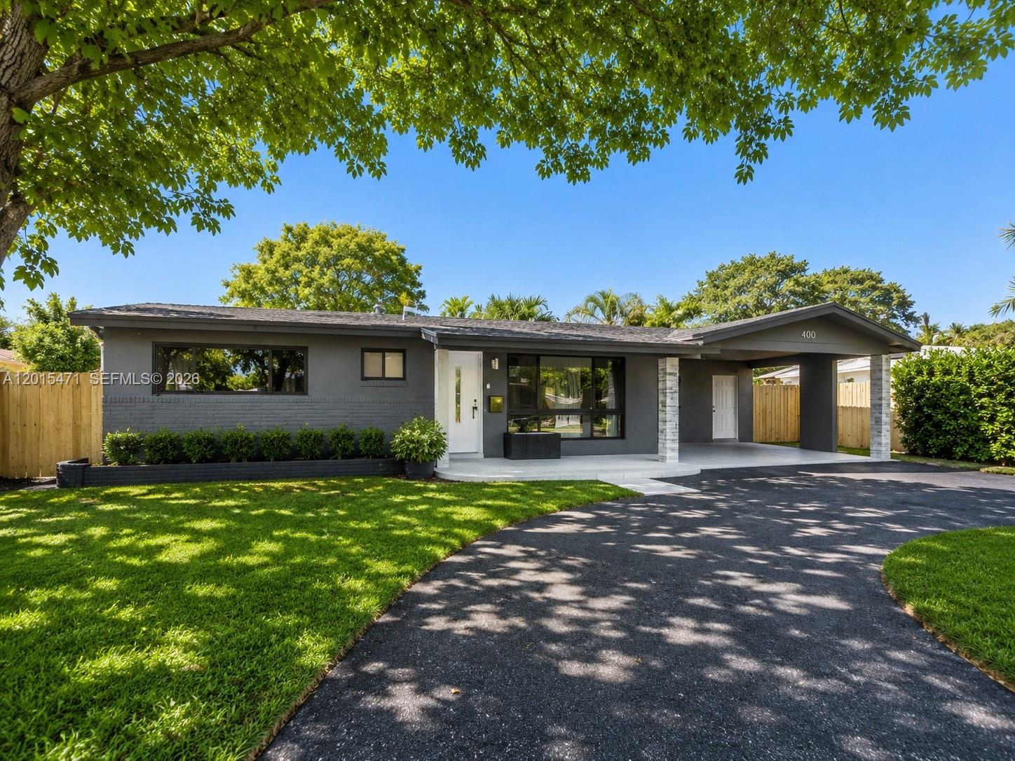 A single-story gray house features a carport, a paved driveway, and a manicured lawn — 400 NW 30th Ct, Wilton Manors FL 33311, WILTON MANORS, FL