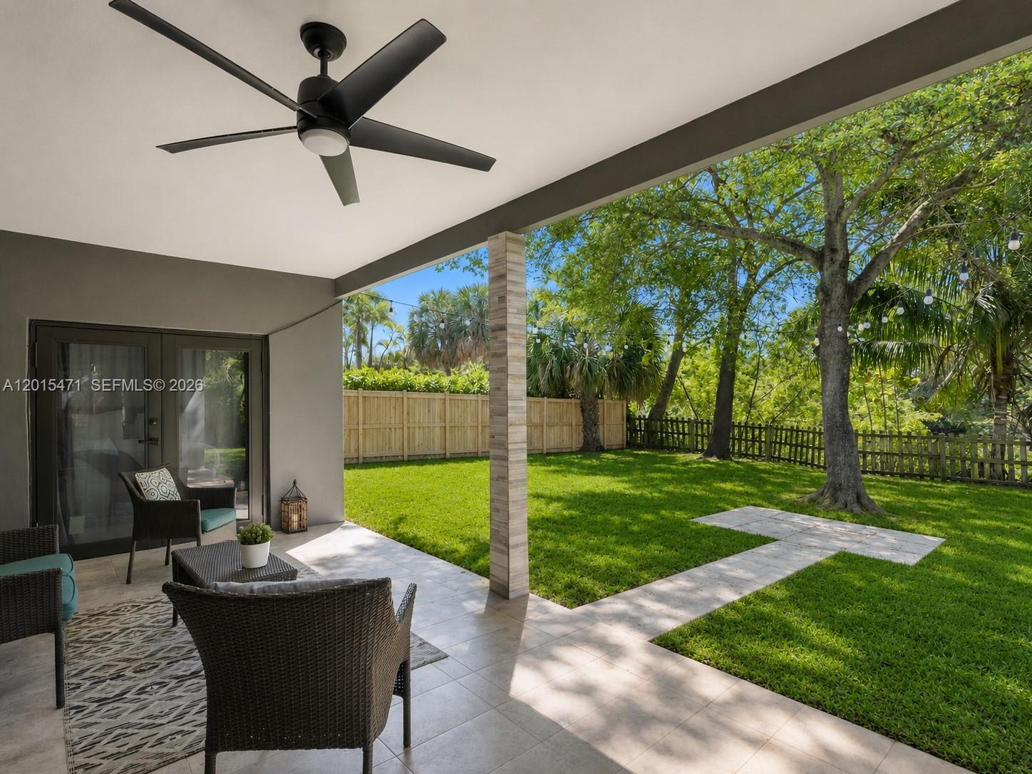 A covered patio with a ceiling fan overlooks a fenced backyard with a large tree — 400 NW 30th Ct, Wilton Manors FL 33311, WILTON MANORS, FL