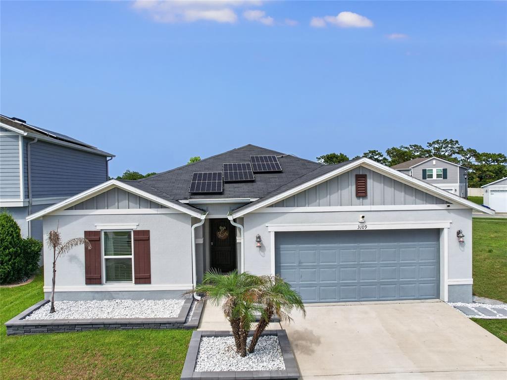 A single-story house with a gray garage, solar panels on the roof, and landscaped beds — 3109 LAKES CREST AVENUE, ST CLOUD, FL
