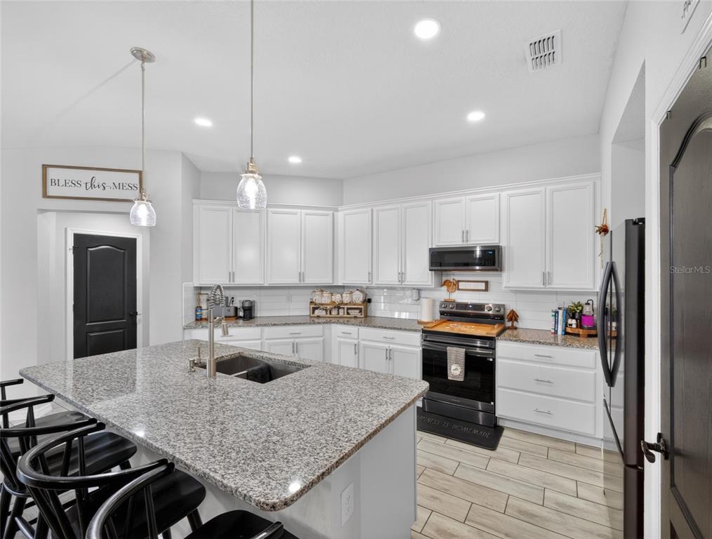 A kitchen featuring white cabinets, granite countertops, a central island, and black appliances — 3109 LAKES CREST AVENUE, ST CLOUD, FL