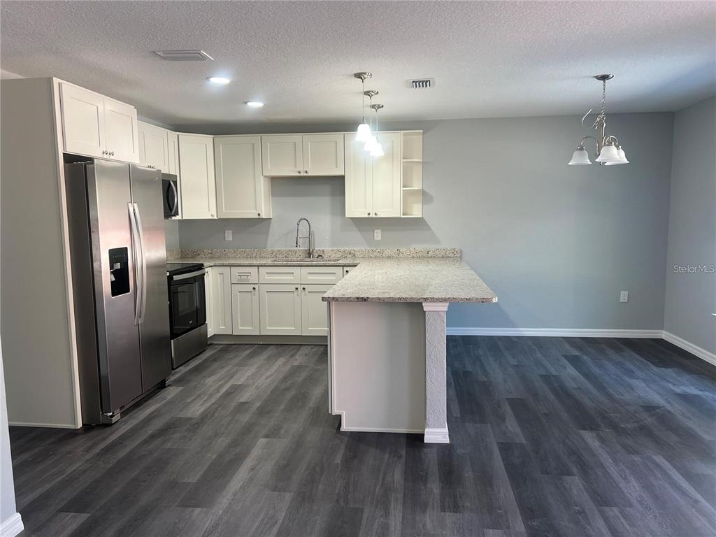 A kitchen features white cabinets, granite countertops, stainless steel appliances, and dark wood-look flooring — 2190 NW 65TH PLACE, OCALA, FL