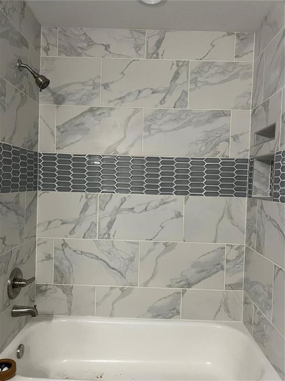 A bathtub shower combination features white marble-look wall tiles and a gray picket-style accent border — 2190 NW 65TH PLACE, OCALA, FL