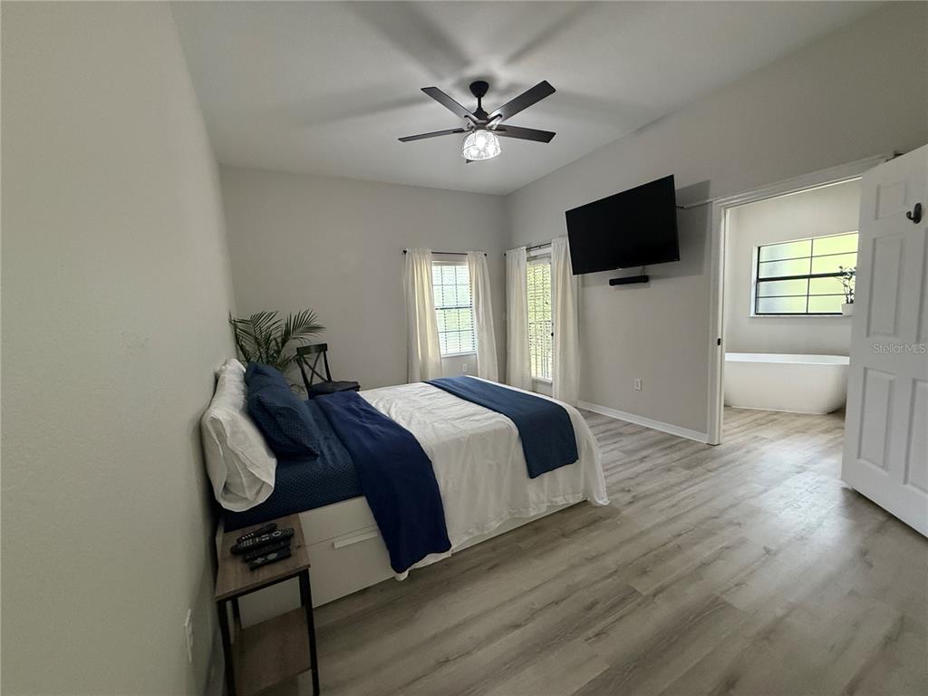 A bedroom features light wood-look flooring, a ceiling fan, a bed, and an attached bathroom — 3060 PIRATES RETREAT COURT UNIT 102, KISSIMMEE, FL