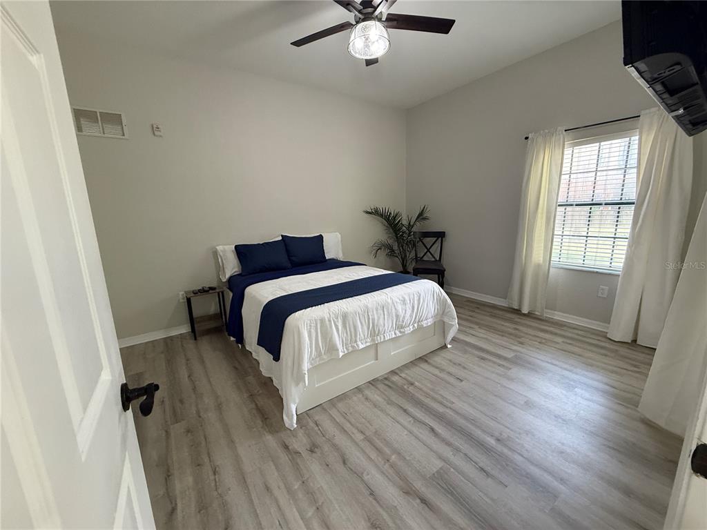 A bedroom features light wood-look flooring, a bed with blue bedding, and a ceiling fan — 3060 PIRATES RETREAT COURT UNIT 102, KISSIMMEE, FL