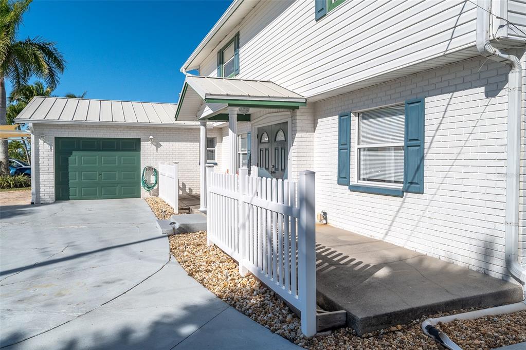 A white brick house exterior features a green garage door, white fence, and front porch — 610 PAULA AVENUE, MERRITT ISLAND, FL