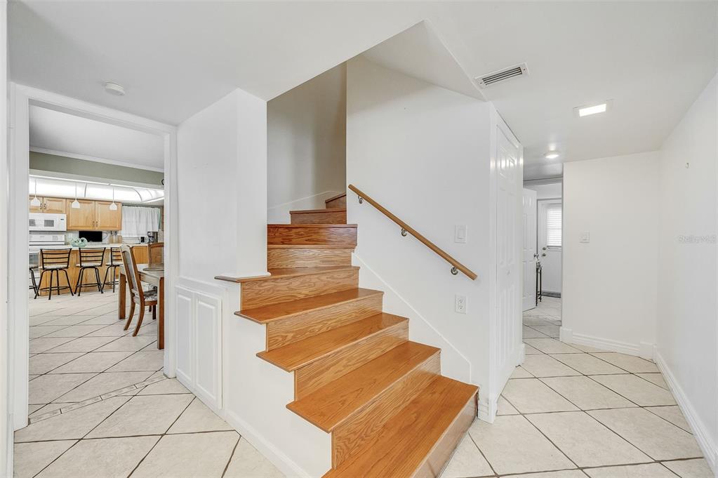 A staircase with wood treads and a handrail sits between a tiled entryway and kitchen — 610 PAULA AVENUE, MERRITT ISLAND, FL
