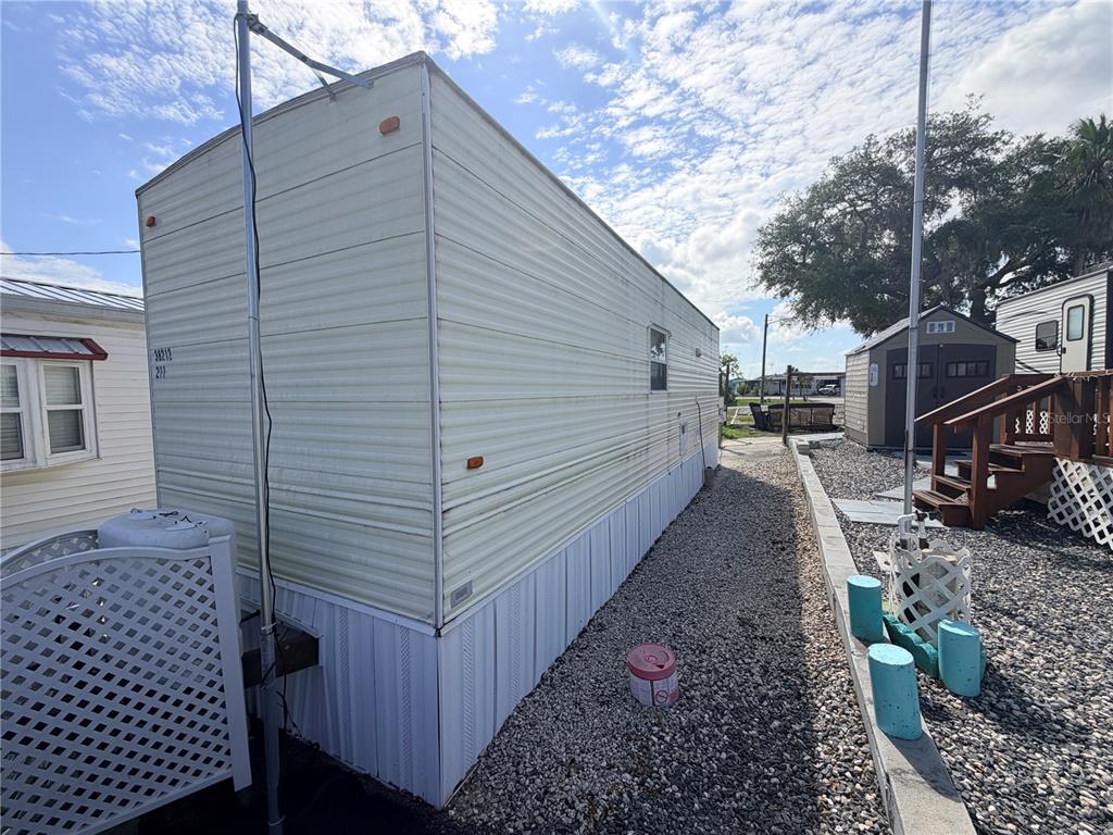 The exterior side of a light-colored mobile home sits next to a gravel walkway — 38212 KINGBIRD WAY, LEESBURG, FL