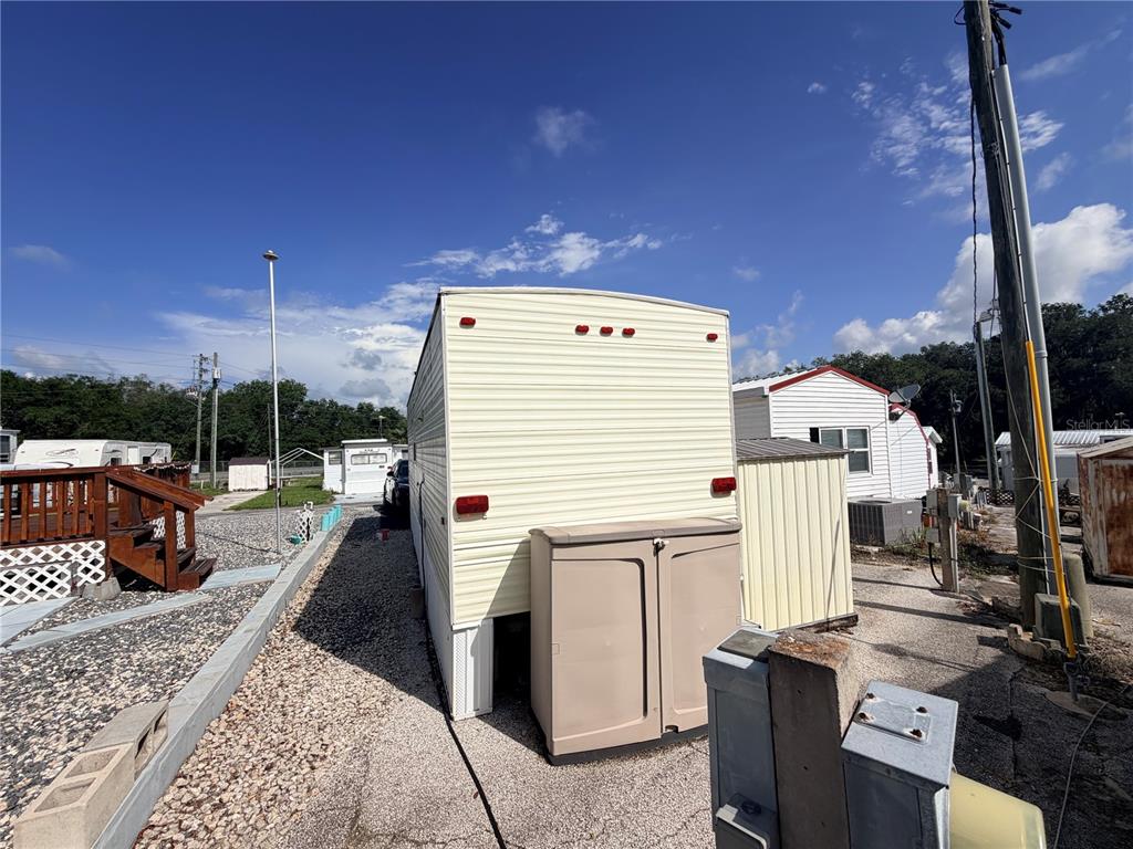 The exterior rear view of a mobile home features light siding and a storage shed — 38212 KINGBIRD WAY, LEESBURG, FL