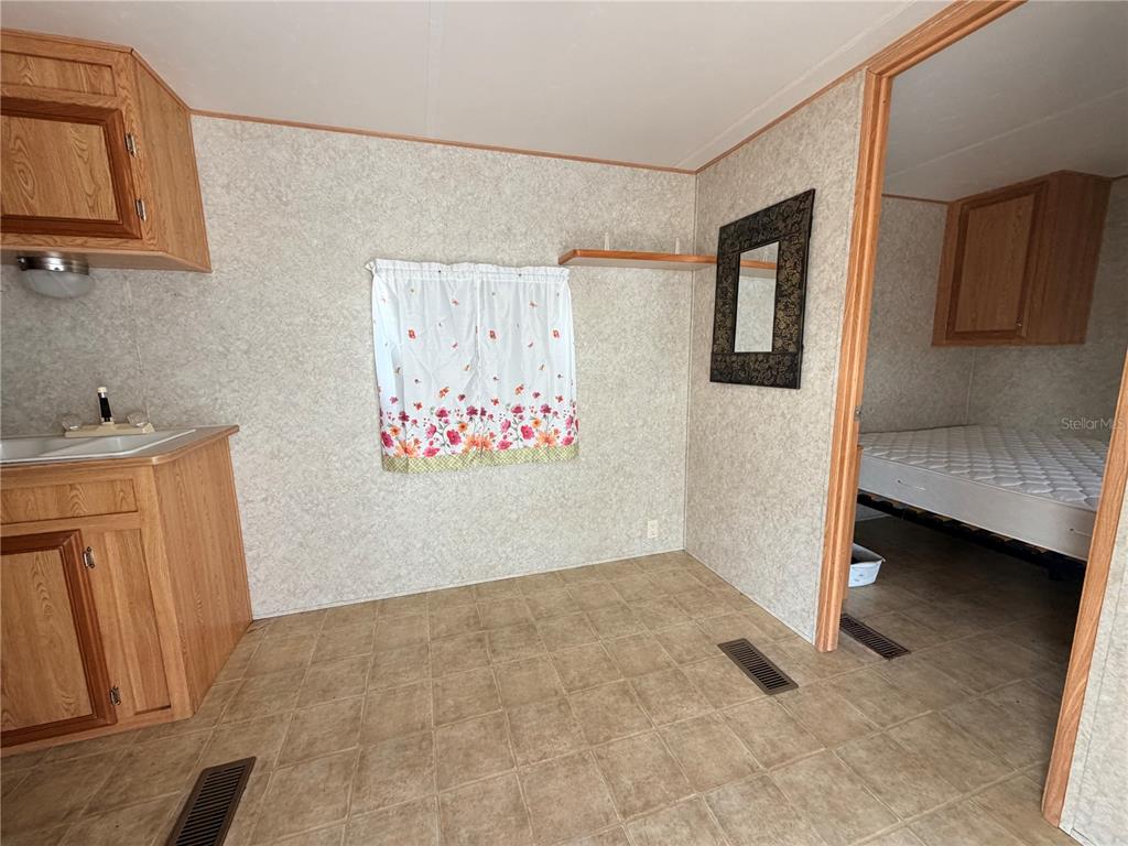 A kitchen area with wood cabinets and vinyl flooring leads into a bedroom with a mattress — 38212 KINGBIRD WAY, LEESBURG, FL