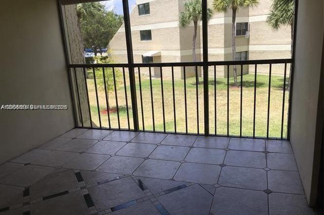 A screened-in balcony with tiled flooring overlooks a grassy courtyard and a neighboring apartment building — 220 Lakeview Dr # 203, Weston FL 33326, WESTON, FL