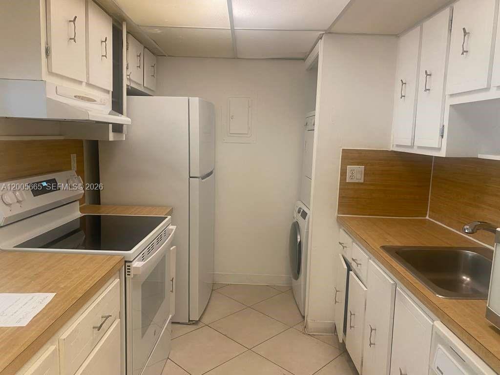 A galley-style kitchen features white cabinets, light wood countertops, a white refrigerator, and a washer-dryer — 220 Lakeview Dr # 203, Weston FL 33326, WESTON, FL