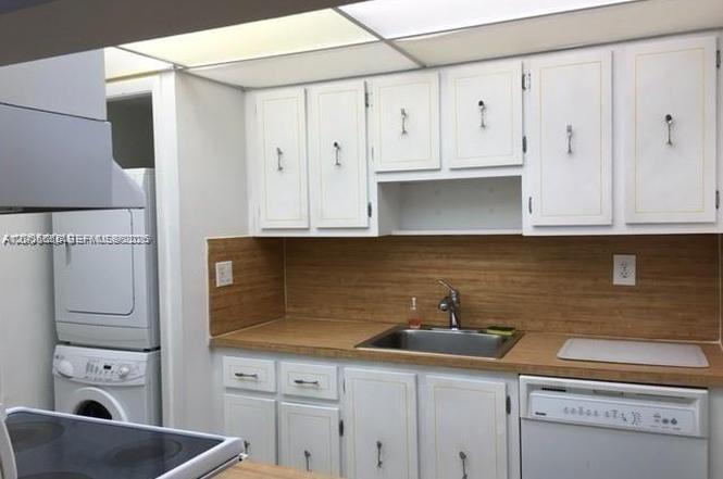 A kitchen features white cabinets, a wood-look backsplash, a stainless steel sink, and stacked laundry — 220 Lakeview Dr # 203, Weston FL 33326, WESTON, FL