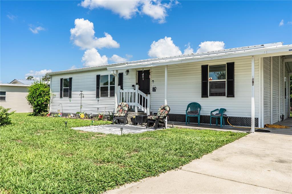 A white single-story mobile home features a front porch, a concrete patio, and a carport — 487 LINDSEY DRIVE, LAKELAND, FL