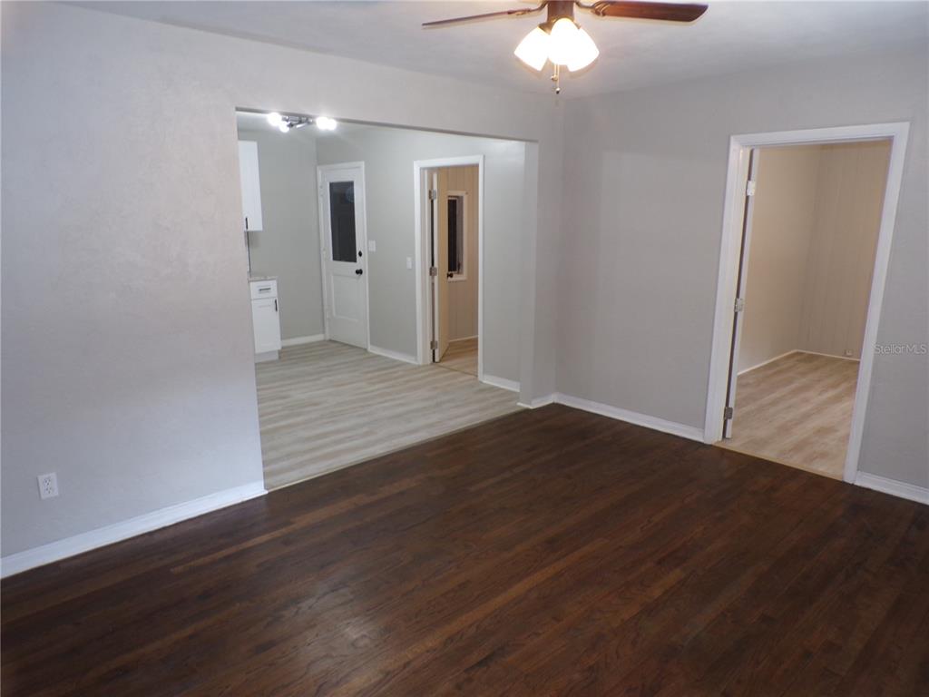 A living room with dark wood flooring leads to a kitchen and an adjacent room — 4402 73RD STREET N, ST PETERSBURG, FL