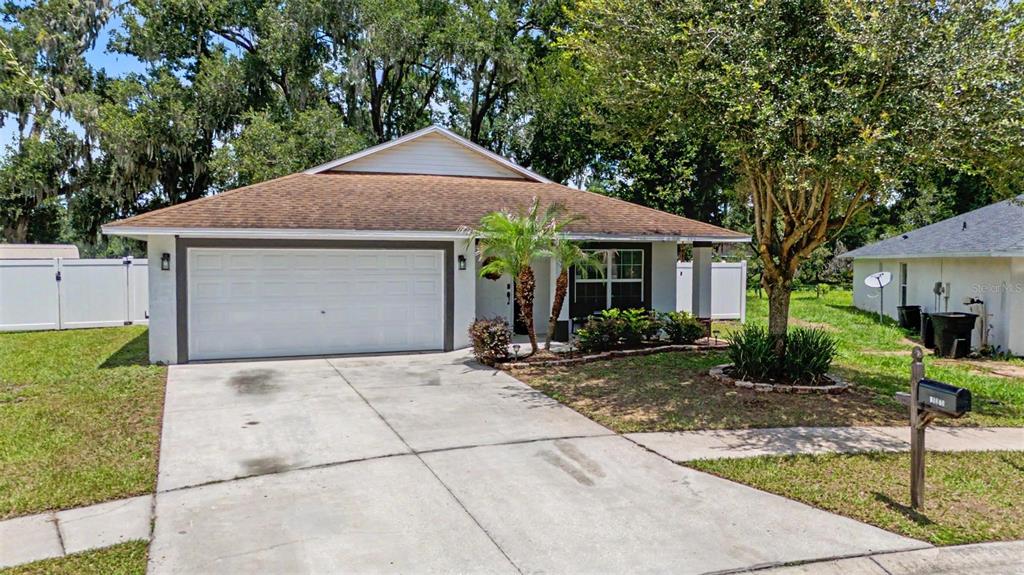 A single-story house with a white garage door, a concrete driveway, and surrounding trees — 15373 CALLISTA LANE, DADE CITY, FL