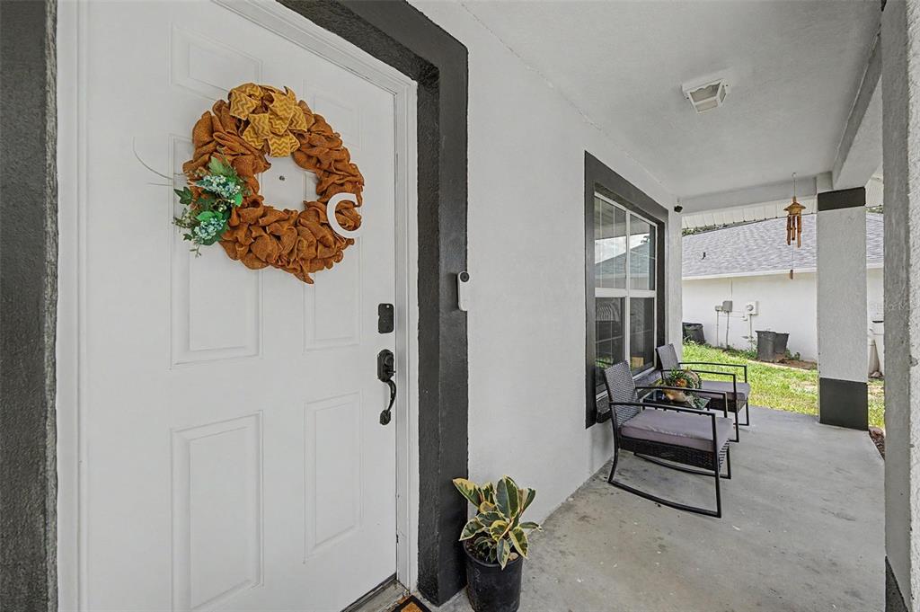 A white front door with a wreath and a covered porch with two chairs — 15373 CALLISTA LANE, DADE CITY, FL