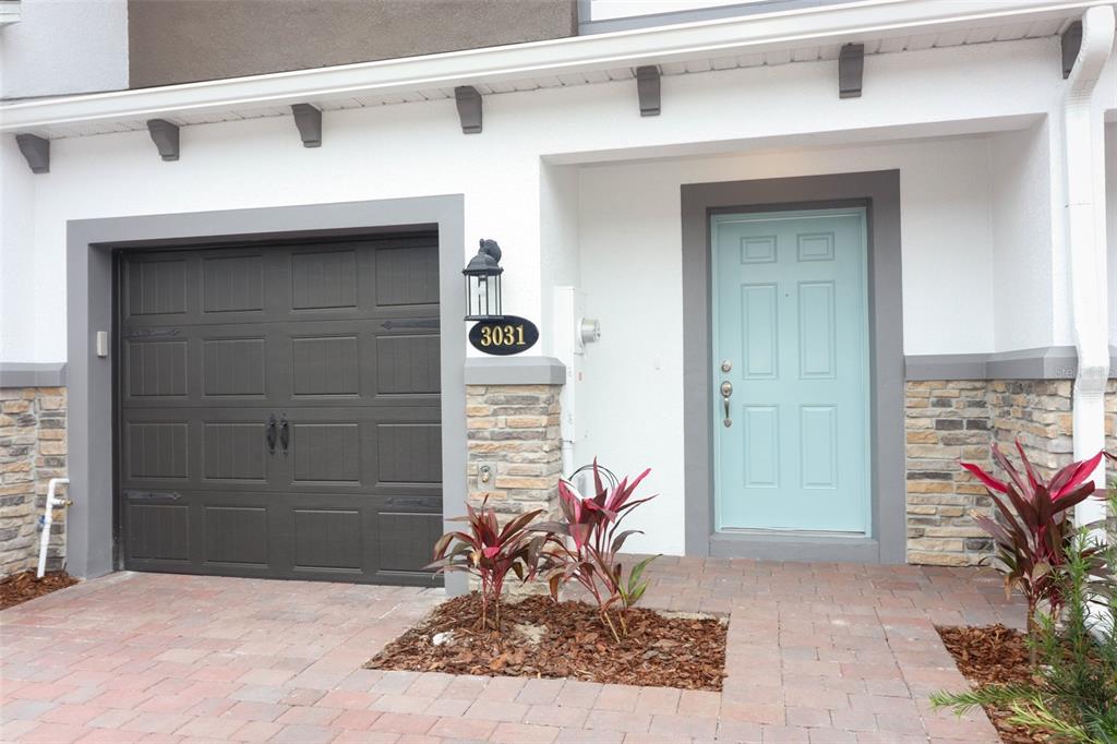 A townhouse exterior features a dark garage door, a light blue front door, and stone accents — 3031 PILOT HOUSE PLACE, OVIEDO, FL