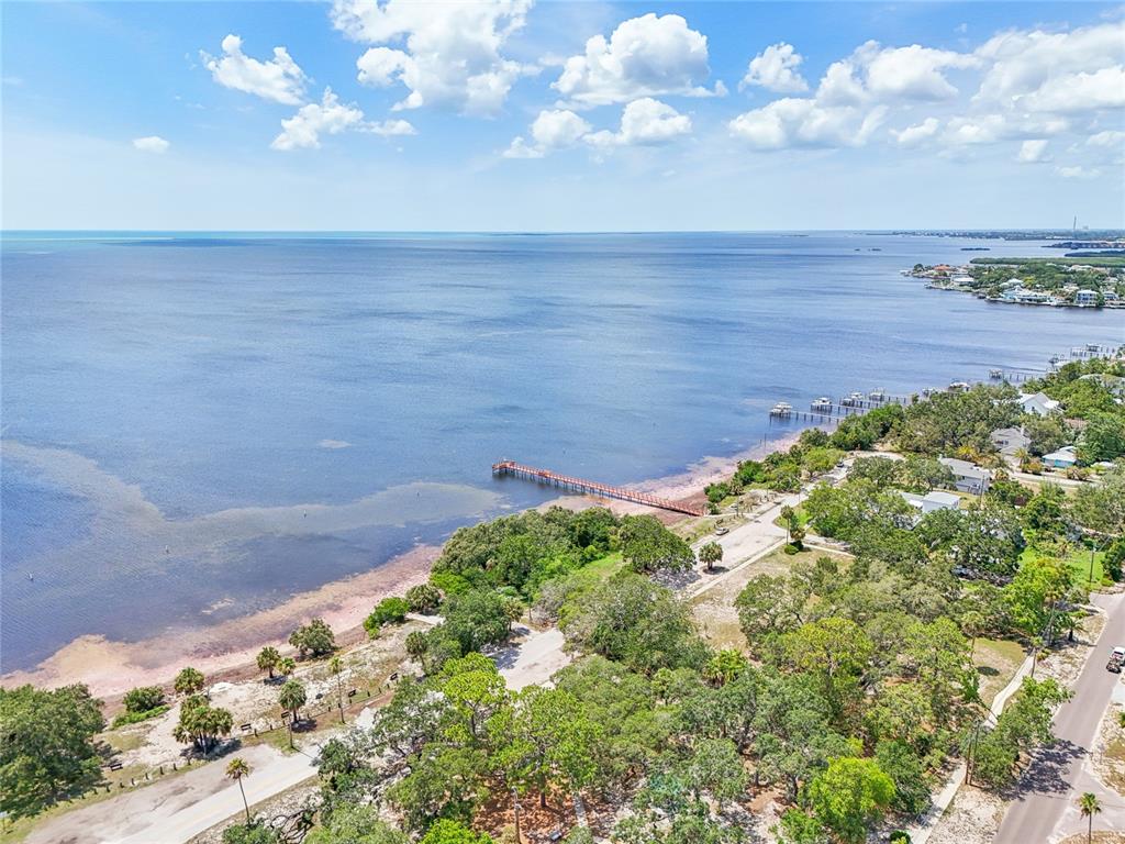 An aerial view shows a long wooden pier extending into a large, calm bay — 131 PENNSYLVANIA AVENUE, PALM HARBOR, FL