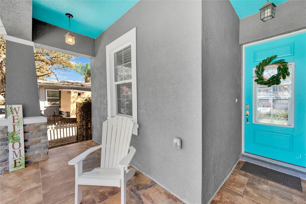 A covered porch features a white chair, a turquoise door, and a welcome sign — 131 PENNSYLVANIA AVENUE, PALM HARBOR, FL