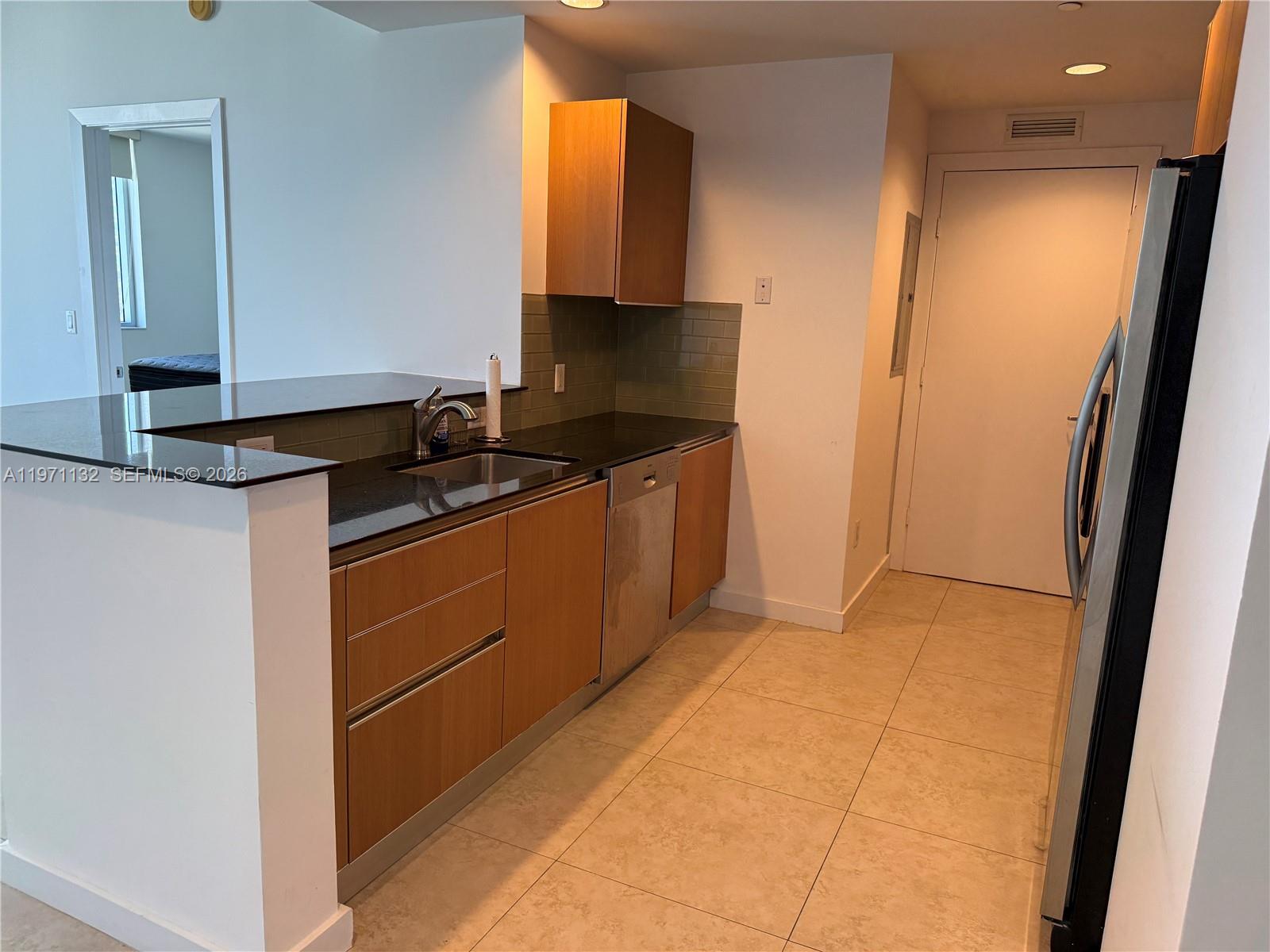 A kitchen features wood cabinets, black countertops, a stainless steel dishwasher, and tile flooring — 1060 Brickell Ave # 3105, Miami FL 33131, MIAMI, FL
