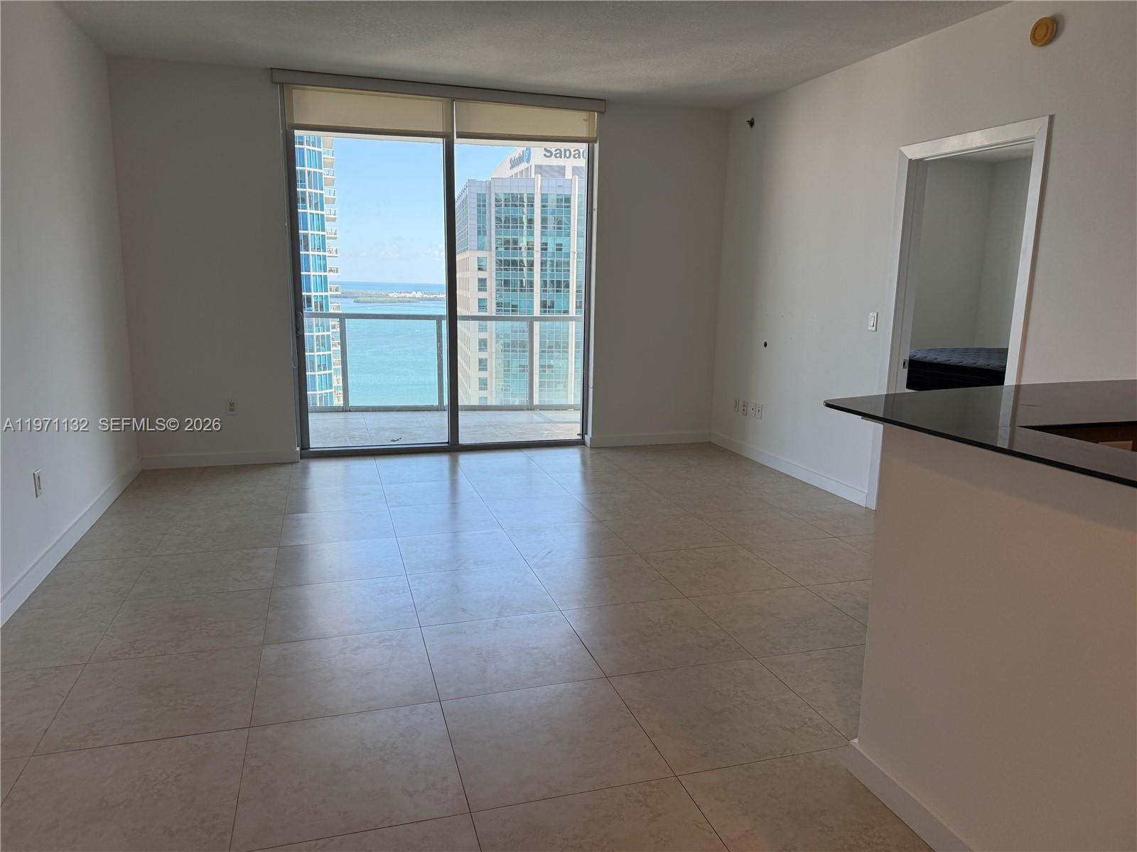 An empty living room features large tile flooring, a sliding glass door, and a balcony view — 1060 Brickell Ave # 3105, Miami FL 33131, MIAMI, FL